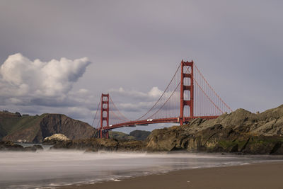 Golden gate bridge over sea against cloudy sky