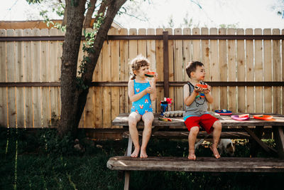 Brother and sister sitting on picnic table eating fresh watermelon