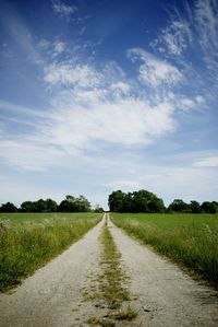 Dirt road amidst grassy field against cloudy sky