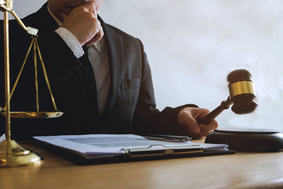 Midsection of lawyer striking gavel on table in courtroom