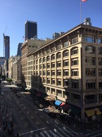 Road by buildings in city against clear sky