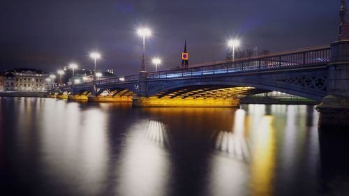 Illuminated bridge over river against sky at night