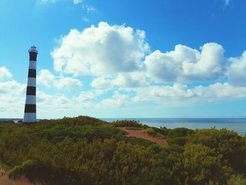 Lighthouse amidst sea and buildings against sky