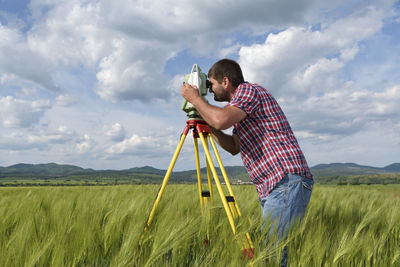 Engineer looking through theodolite on field against sky