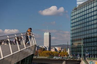 People standing by railing against buildings in city against sky