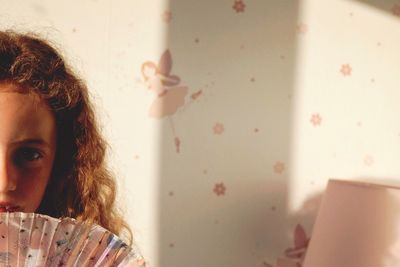 Cropped portrait of girl with hand fan against wall at home