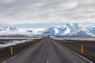 Road by snowcapped mountains against sky