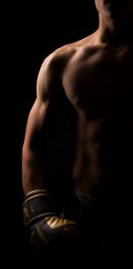 Midsection of shirtless man standing against black background