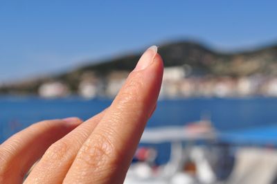 Close-up of hand against sea against sky