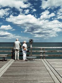 People on pier over sea against sky