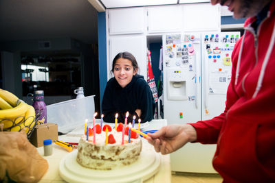 Father lights candles on daughter's cake while she looks excited