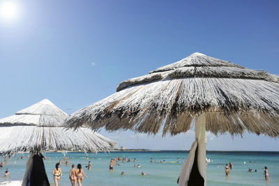 Close-up of thatched roof with people i background at beach against clear blue sky