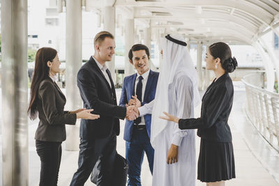 Business people applauding while businessmen giving handshake in office corridor