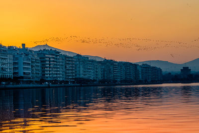 Buildings by river against sky during sunset