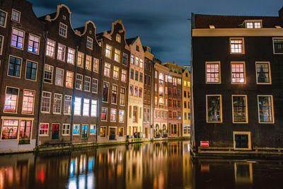 Buildings in city by river against cloudy sky