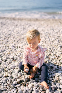 Full length of cute boy sitting on rock at beach