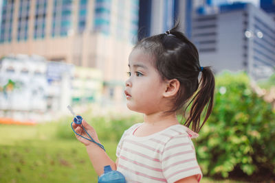 Side view of cute girl holding bubble wand while looking away in park