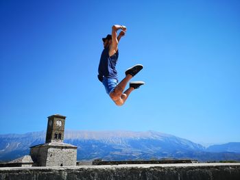 Full length of man jumping against blue sky