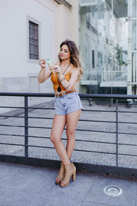 Young woman having ice cream while standing by railing in city