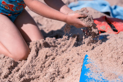 Close-up of girl playing with sand at beach during summer