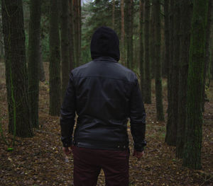 Rear view of man standing by trees in forest