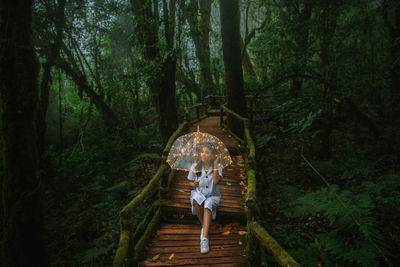 Woman sitting with umbrella on boardwalk in forest