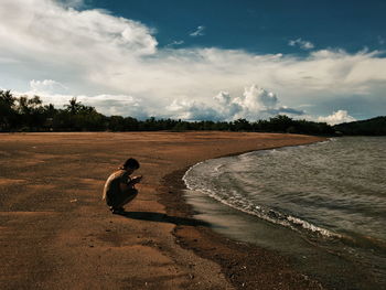 Side view of man sitting on land against sky