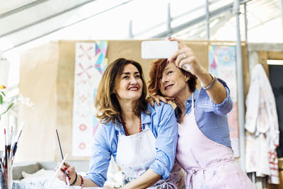 Cheerful mature workshop owners taking selfie while creating goods