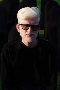 Portrait of the albino man sitting on the black chair wearing glasses