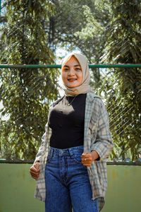 Portrait of smiling young woman standing against trees