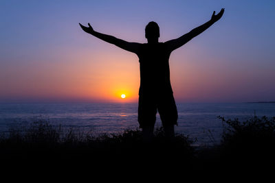 Silhouette person standing by sea against sky during sunset