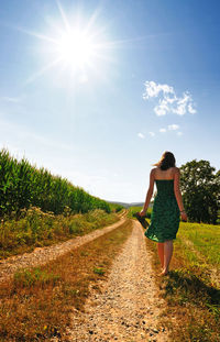 Rear view of woman walking on grass against sky