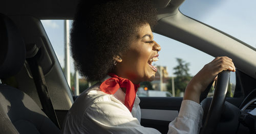 Side view of african american female driver driving automobile and laughing happily with eyes closed