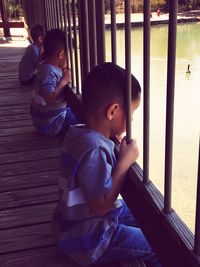 Boys looking at lake while sitting on footbridge