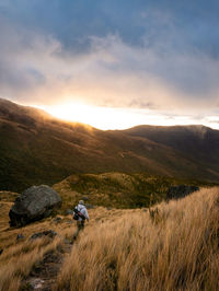 Rear view of man hiking on mountain against sky during sunset