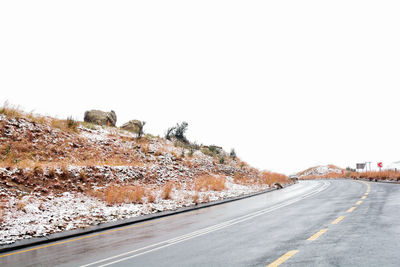 Road by snow covered landscape against clear sky