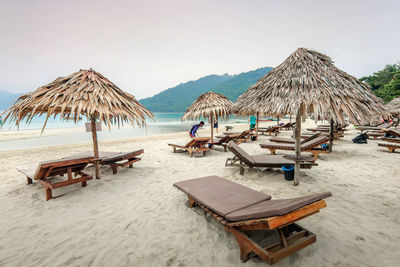 Lounge chairs and parasols on beach against sky