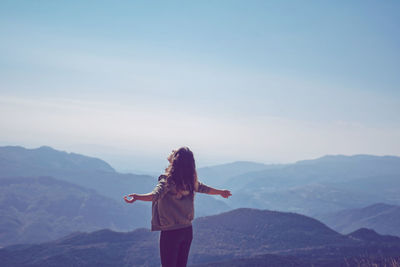 Rear view of woman standing on mountain against sky