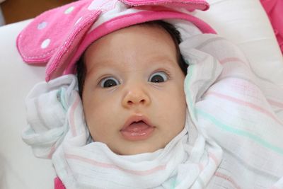 Close-up portrait of shocked baby girl lying on bed