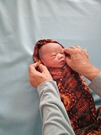 Cropped hands of person wrapping cute baby boy lying on bed at home