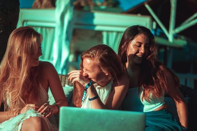 Happy female friends sitting at beach