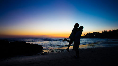 Silhouette couple embracing at beach against sky during sunset