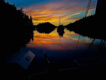 Reflection of silhouette trees on sea against sky during sunset