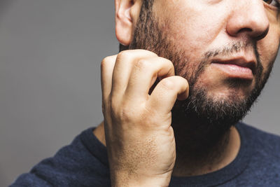 Close-up of man touching beard against gray background