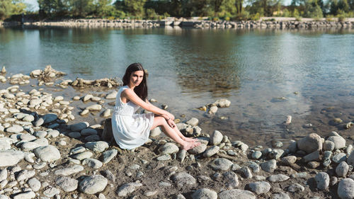 Portrait of young woman sitting on rock by lake