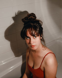 Beautiful young woman against tiled wall in bathroom