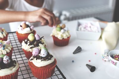 Midsection of person garnishing cupcakes on table at home