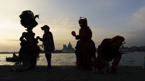 People wearing costume at beach against sky during sunset