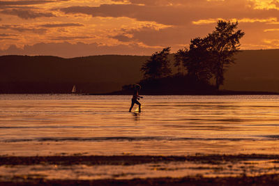 Silhouette person on sea against sky during sunset