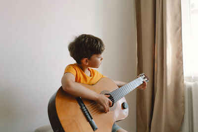 Cute boy learns to play the classical guitar in home. cozy home.